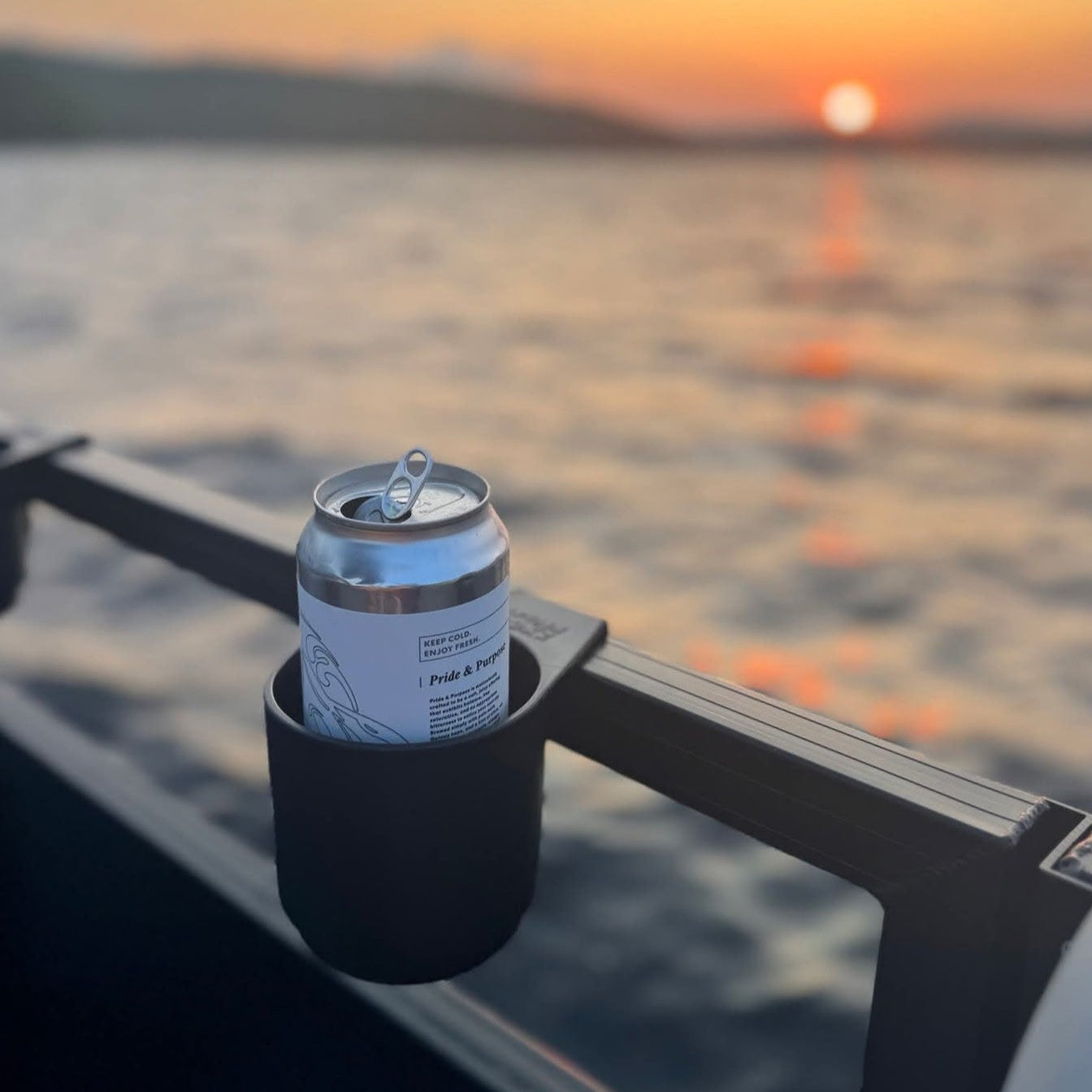 Drink in a cup holder on a pontoon boat with a sunset over water in the background